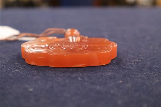A Chien Lung red bowenite, carved and shaped disc pendant, decorated with stylised scrolls